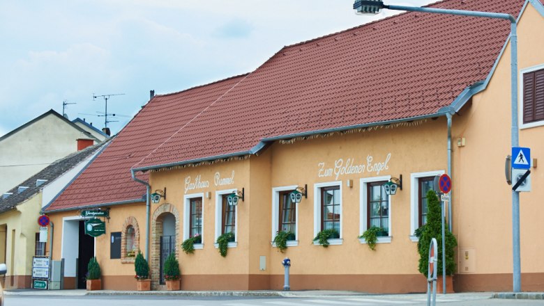 Ein traditionelles Gasthaus mit gelber Fassade und rotem Dach, beschriftet mit 'Gasthaus Rammel' und 'Zum Goldenen Engel'.