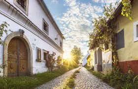 Kopfsteinpflasterstraße in Röschitz mit historischen Gebäuden und Sonnenuntergang.